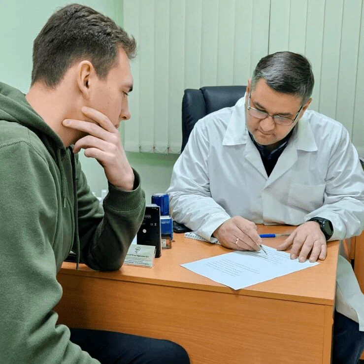Врач беседует с посетителем за столом в кабинете